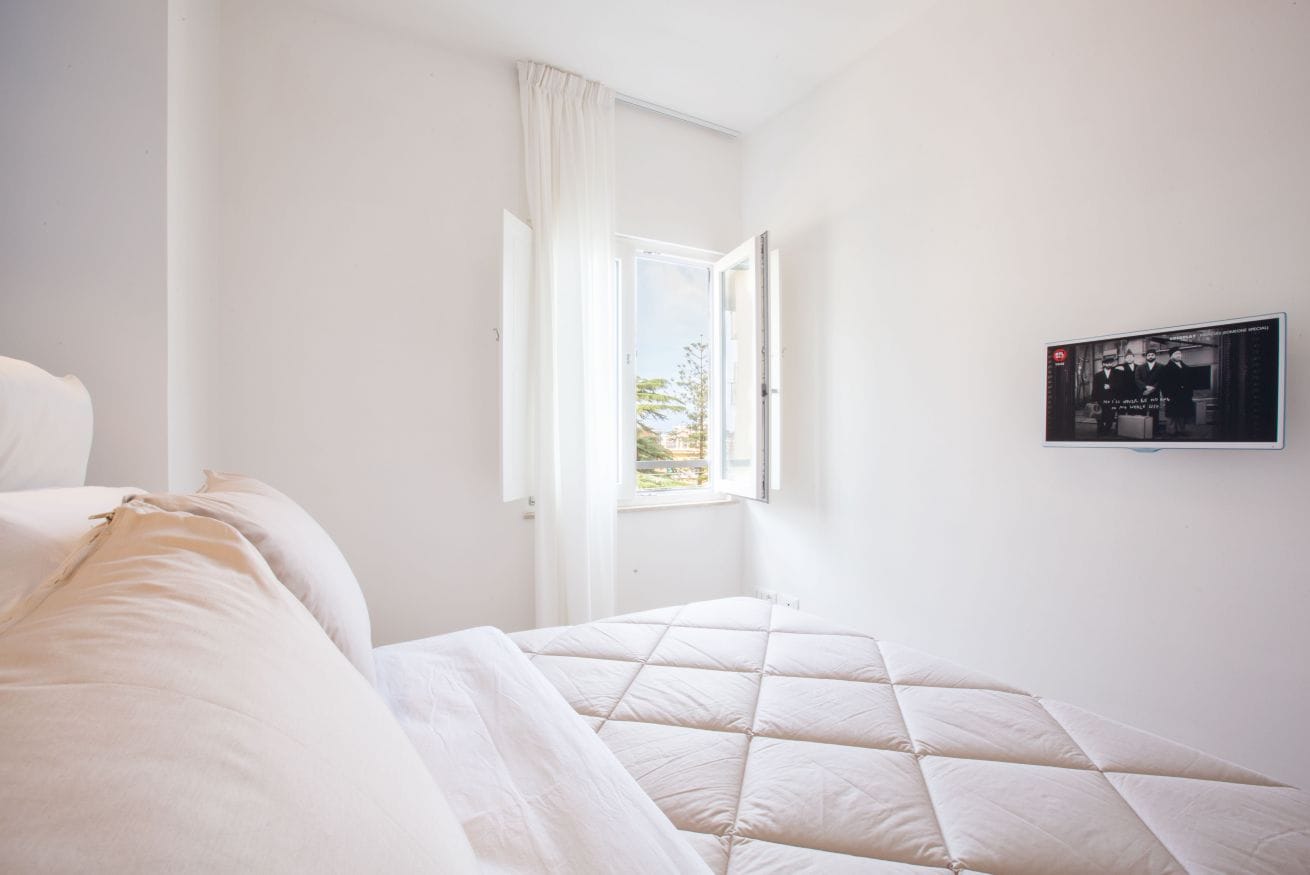 Ein Schlafzimmer mit einem Bett, einem Fenster mit Vorhängen und einem an der Wand befestigten Fernseher.