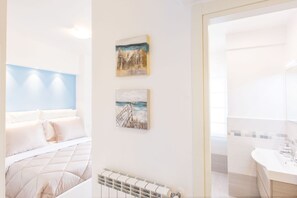 Quarto de hotel com cama, radiador e duas pinturas na parede.