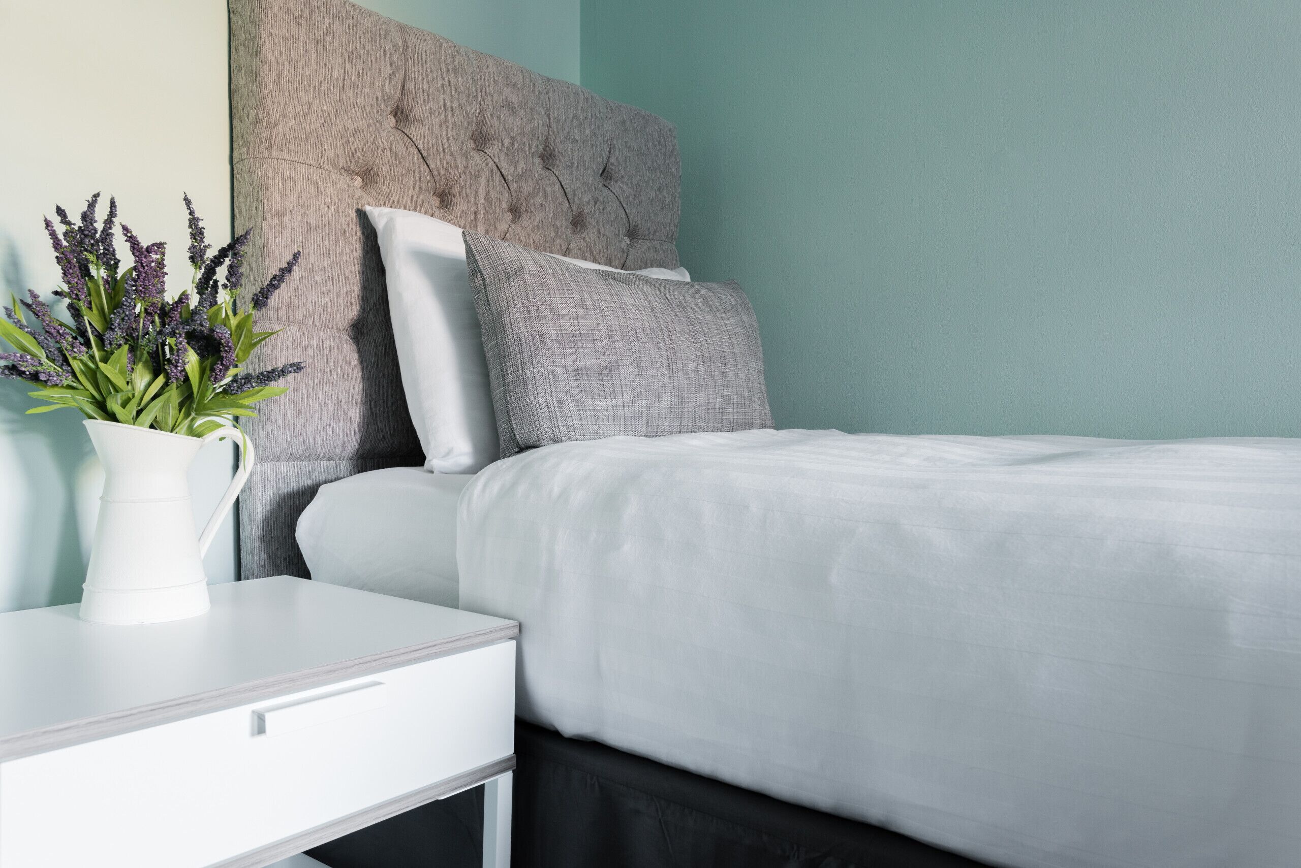 Un dormitorio ordenado con cama, almohadas, una mesita de noche y una planta en maceta.