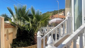 Una escalera con barandillas blancas que conduce a la entrada de un edificio, rodeada de palmeras y un muro de piedra.