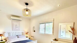 Un dormitorio con cama, escritorio, silla, ventana y aire acondicionado de pared.