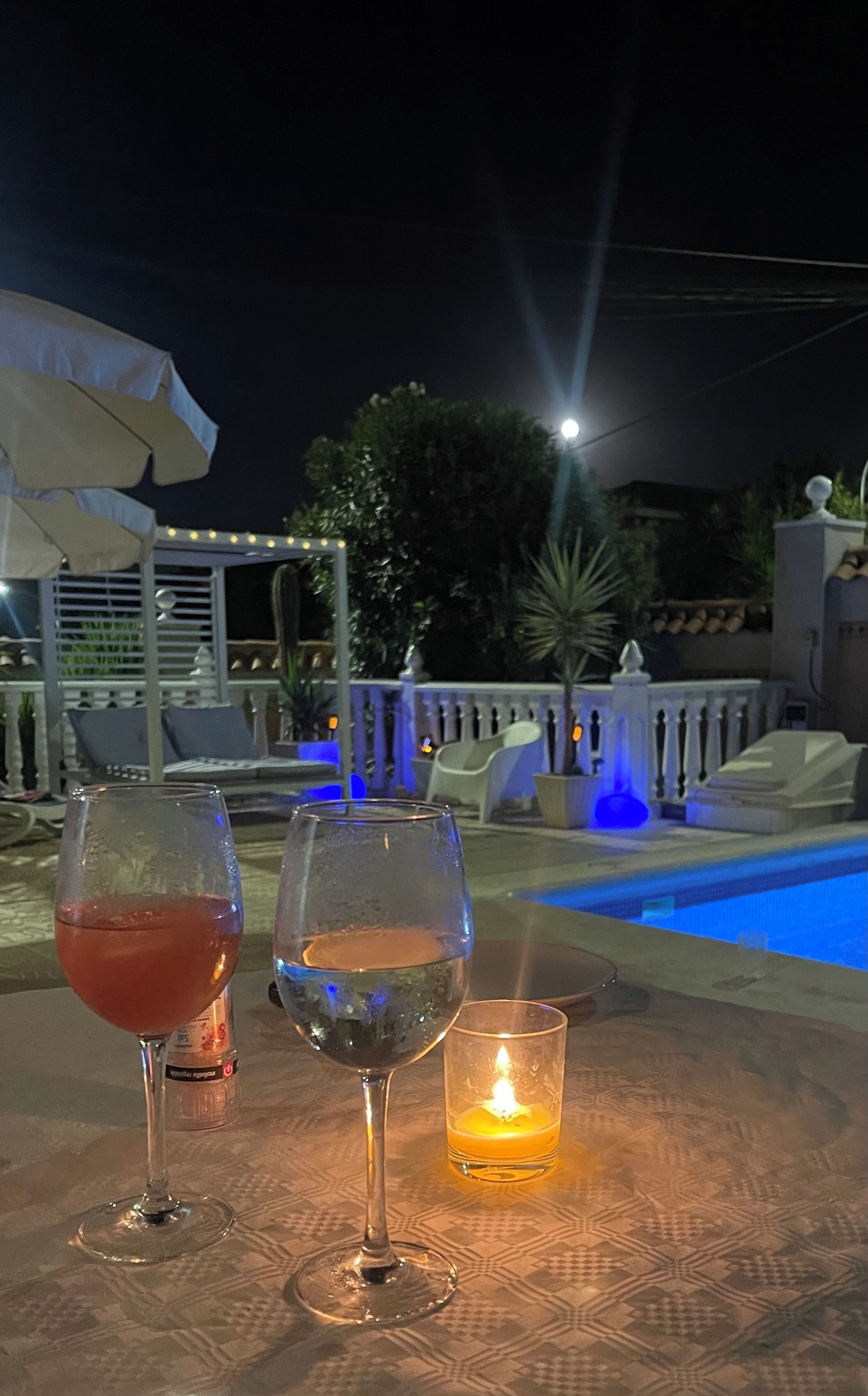 A poolside table with two wine glasses and a candle, surrounded by outdoor seating and a pool.