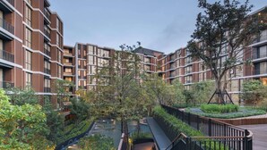 En modern bostadsbyggnad med en central innergård, träpromenader och omgivande grönska.