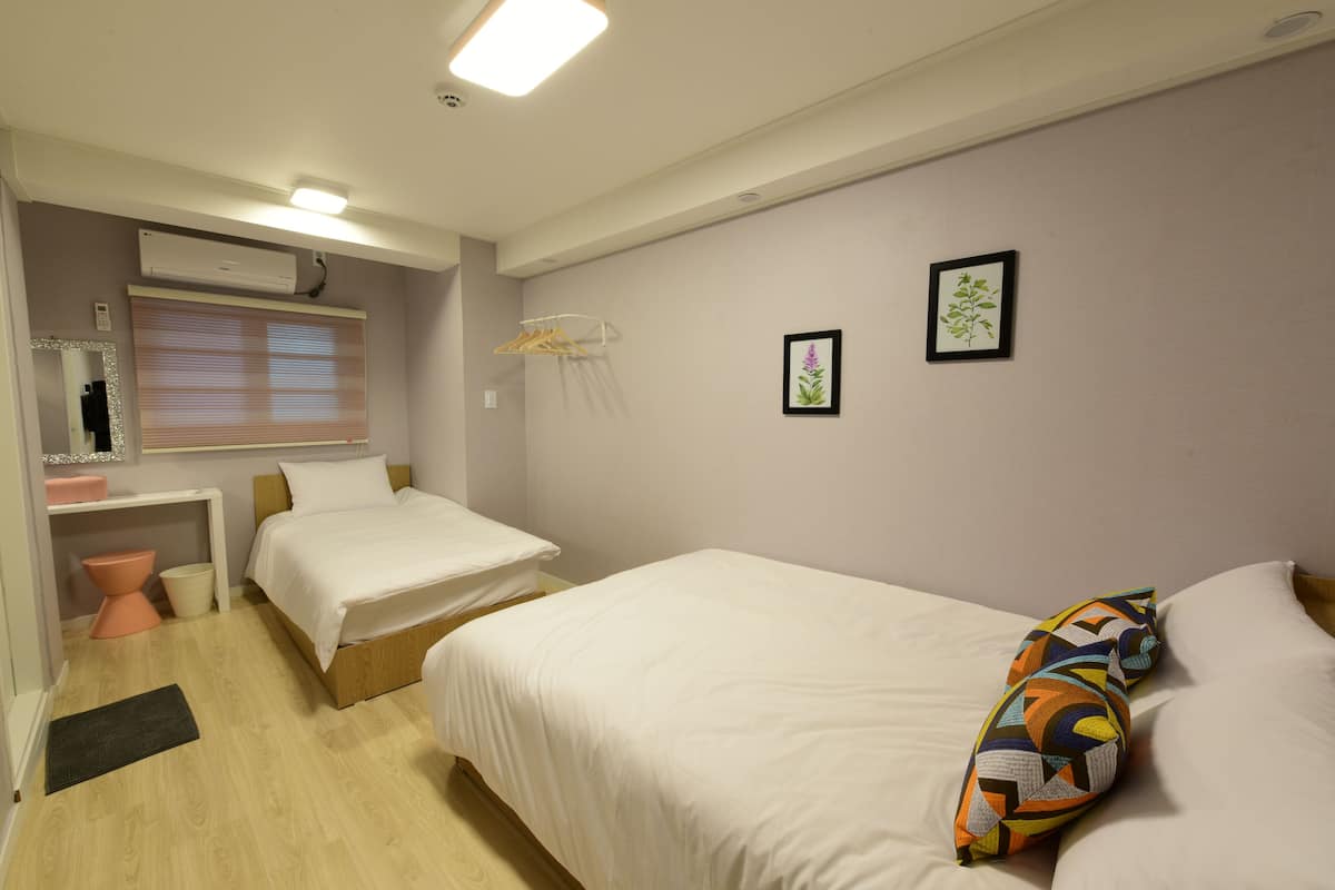 A bedroom with two beds, a bedside table, a mirror, and a window with blinds.