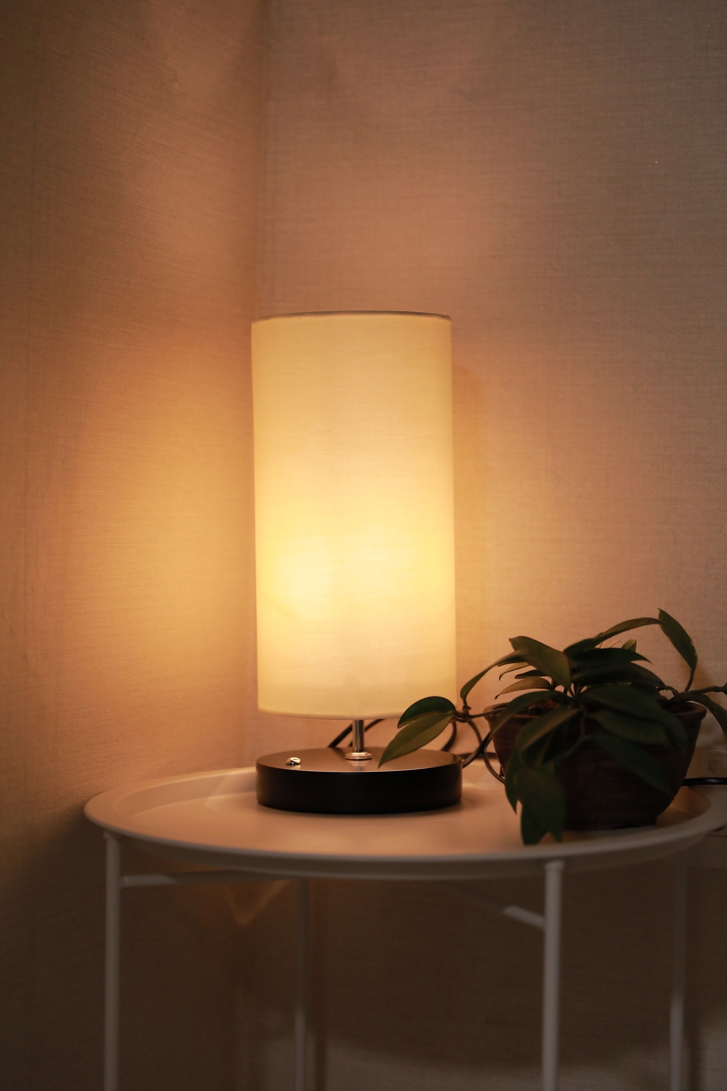 A table lamp with a cylindrical shade on a white table against a textured wall.