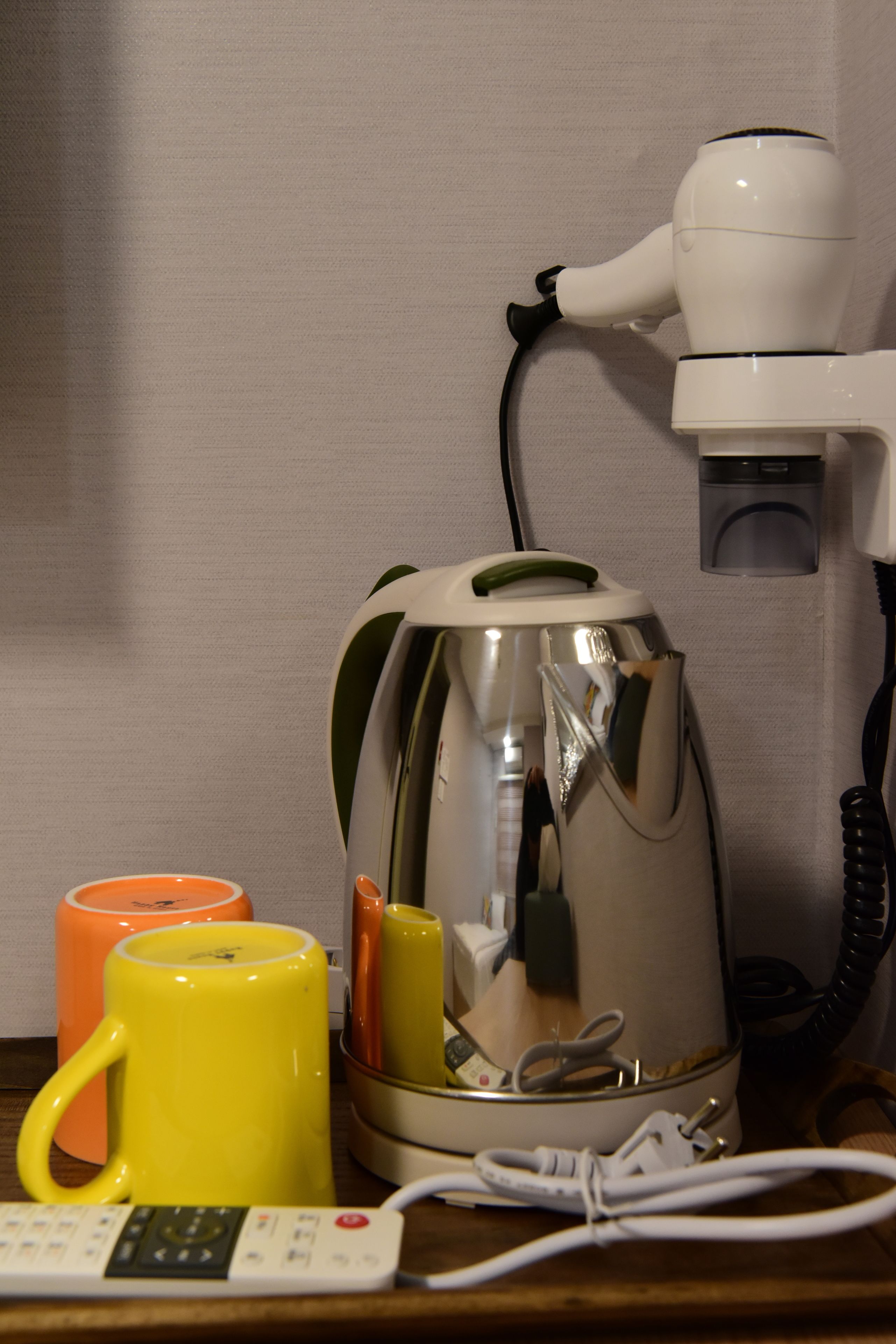 A coffee maker, two mugs, and a telephone on a wooden surface.