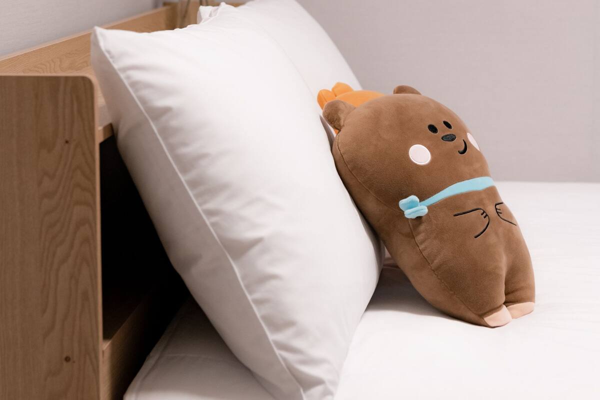 A bed with a white pillow and a brown plush toy.