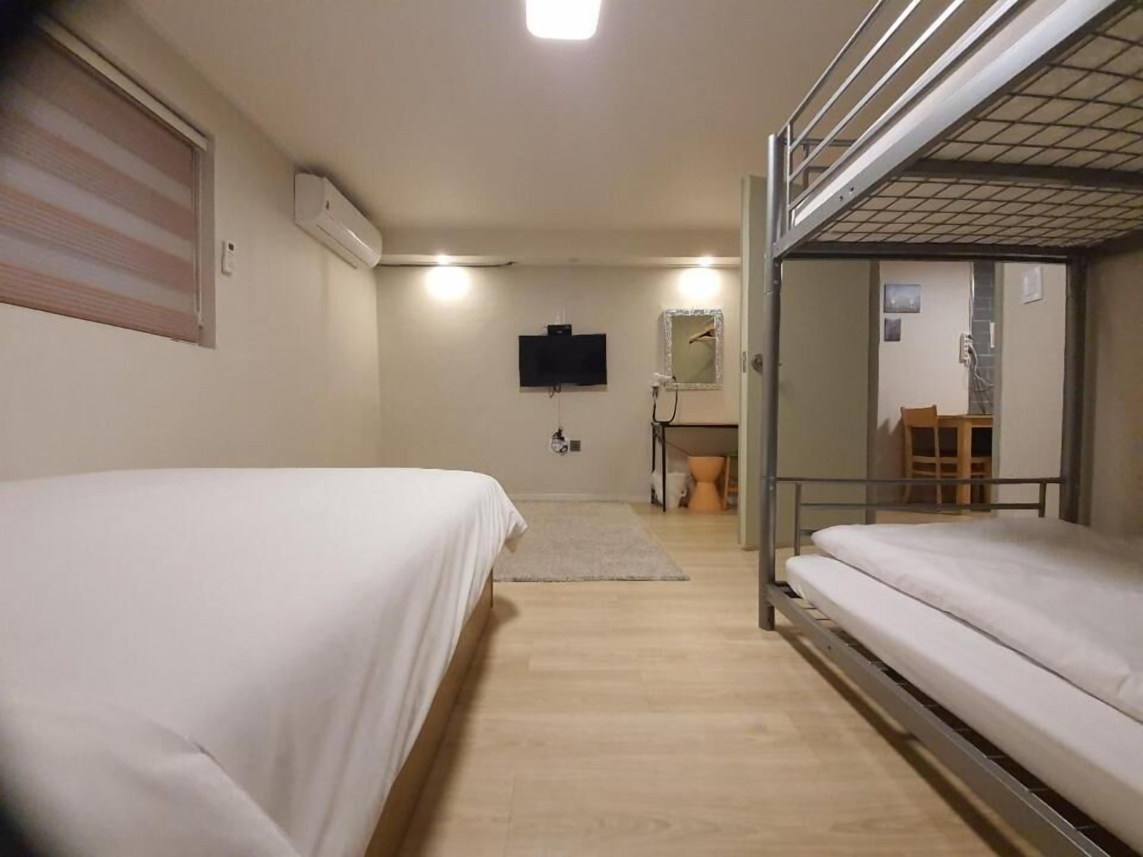 A hotel room with a bed, a bunk bed, a television, a mirror, and a small bathroom.
