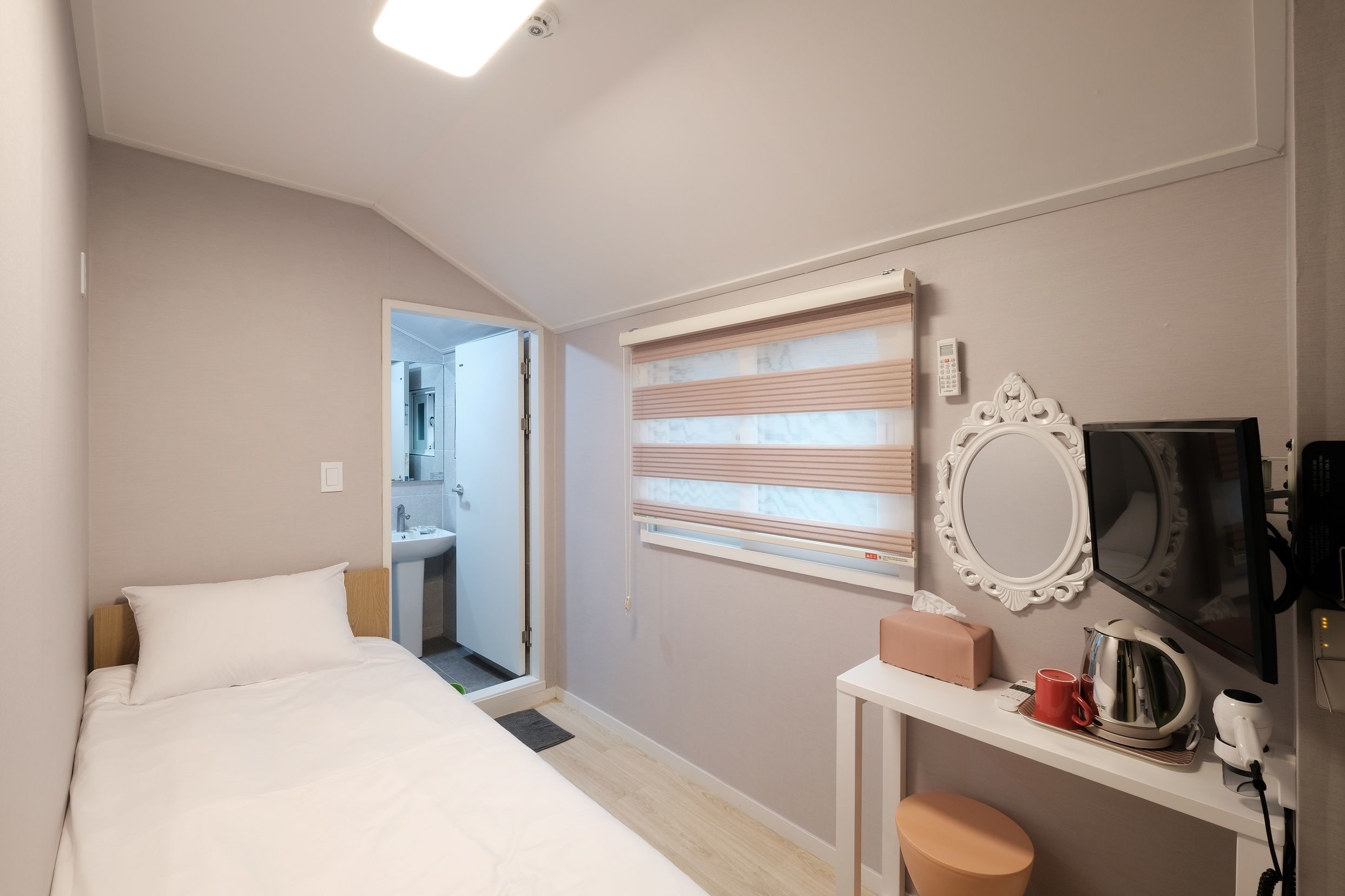 Una habitación de hotel con cama, escritorio con espejo, televisión y ventana con persianas.
