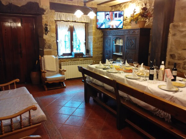 A dining area with a long table set for a meal, a television mounted on the wall, and a stone wall in the background. - Casa con Bodega for 9 people (Sajazarra)