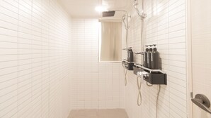 A bathroom with white tiled walls, a shower with a handheld showerhead, and a window with a curtain. - Dawoo House - Hostel (Seoul)