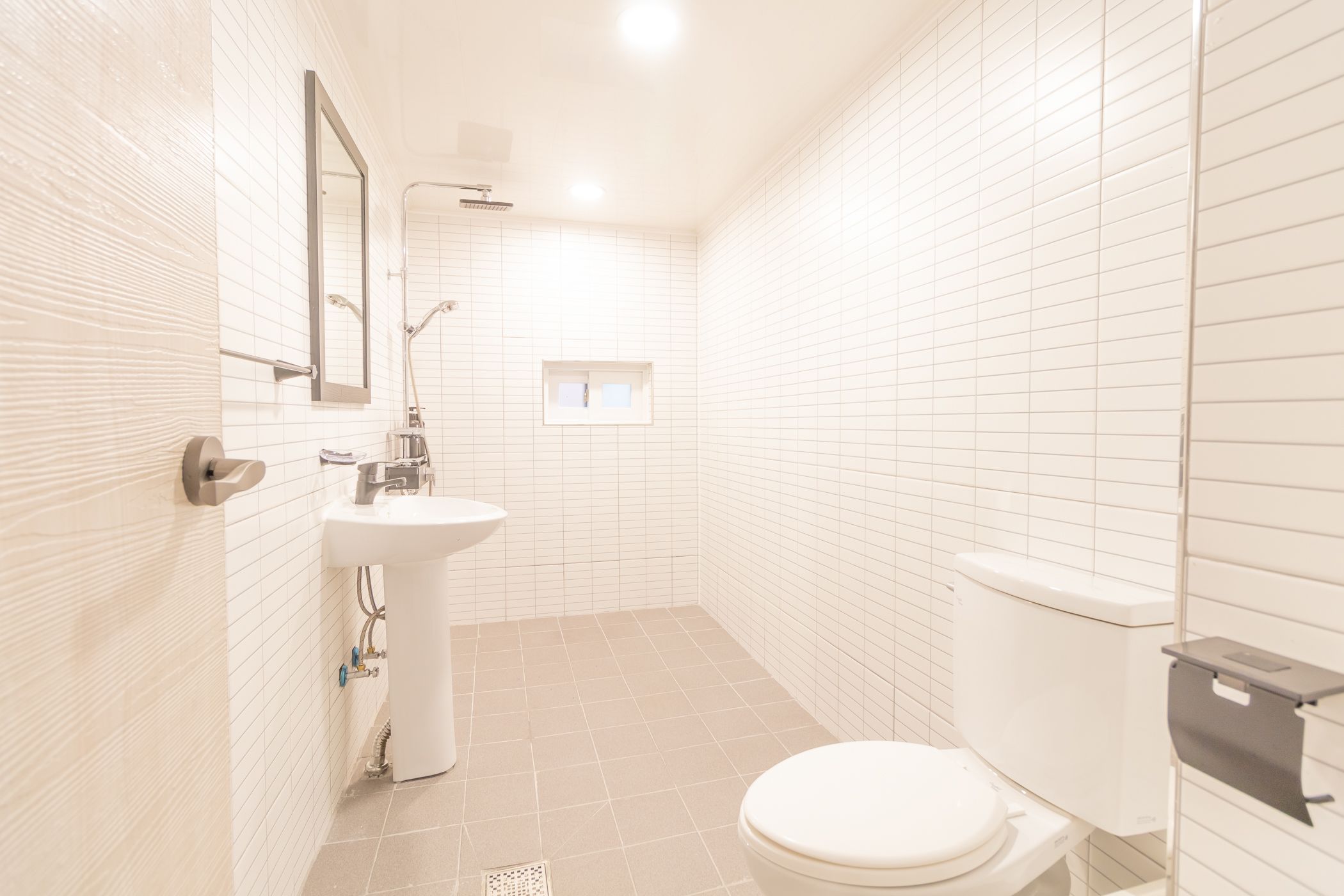 A small, clean bathroom with white tiles, a sink, a toilet, and a mirror.