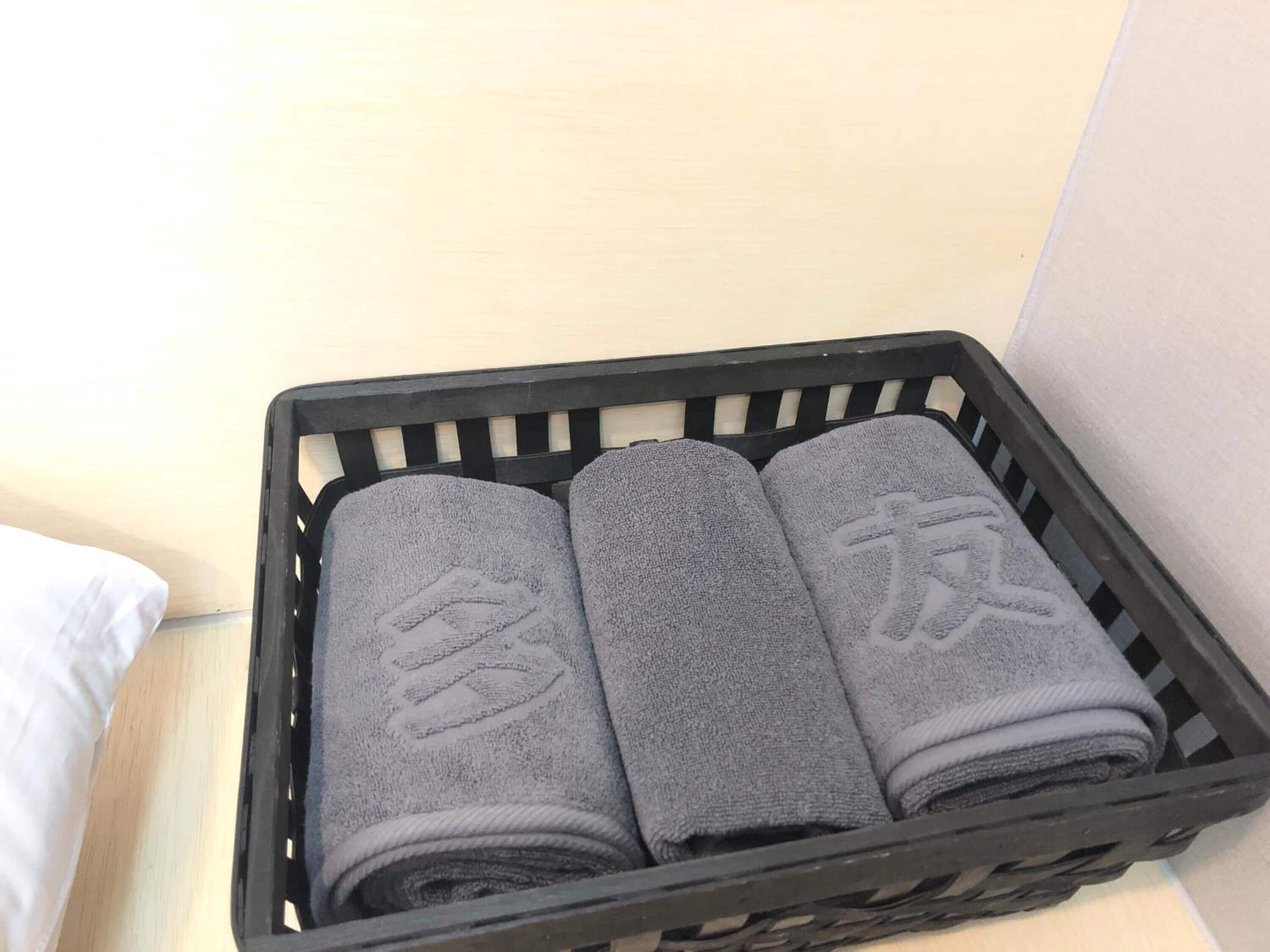 Un panier en plastique noir contenant trois serviettes grises enroulées.