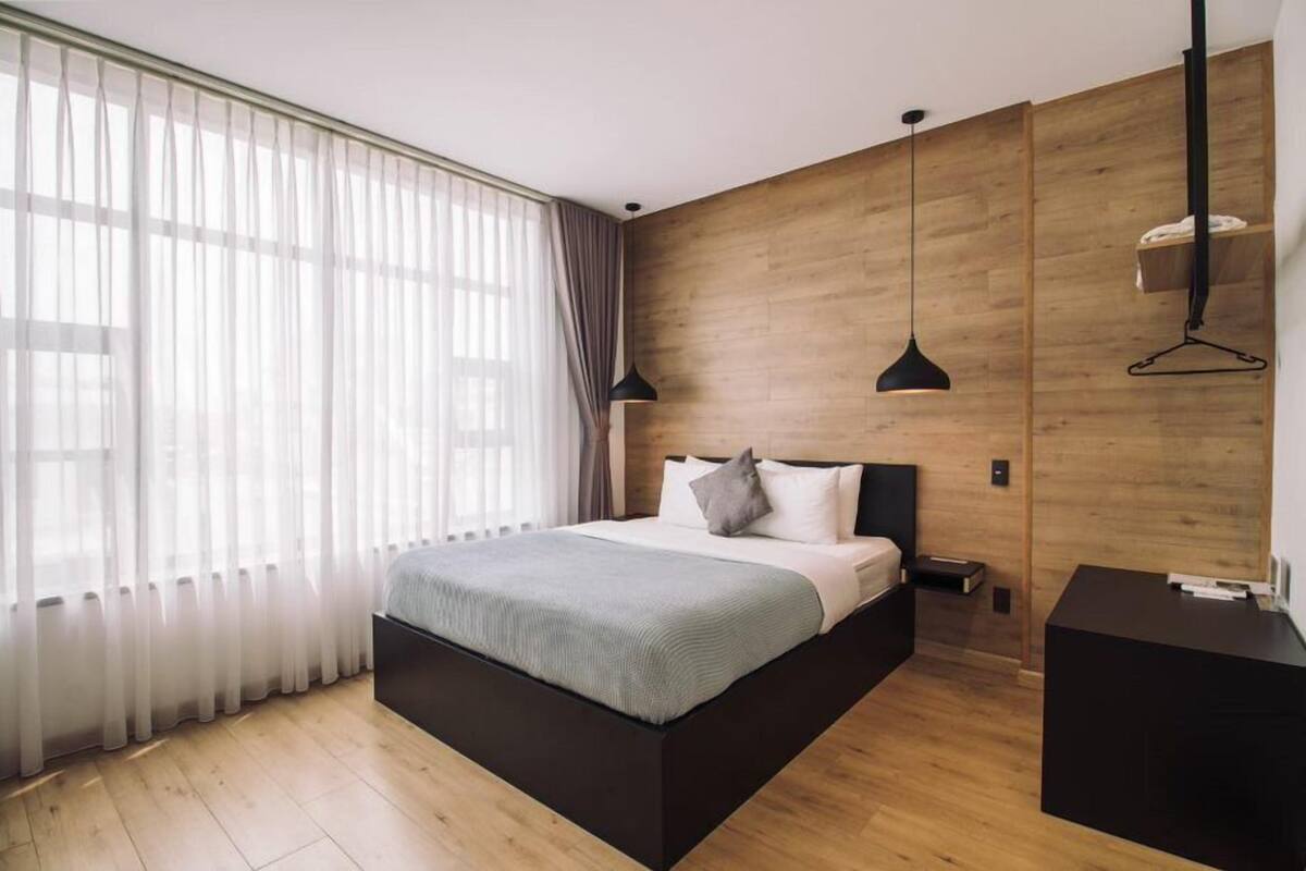 Une chambre moderne avec un grand lit, des murs recouverts de panneaux en bois et une lampe suspendue noire.