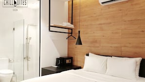 Una habitación de hotel moderna con un cabecero de madera, una cama con ropa blanca, una mesita de noche negra, una lámpara negra y un box de ducha de vidrio.