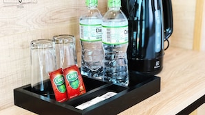 Una bandeja con dos botellas de agua Dasani, dos sobres de té Cozy, dos vasos y una cafetera negra sobre una superficie de madera.
