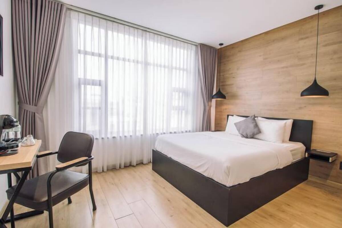 Une chambre d’hôtel moderne dotée d’un grand lit, d’un bureau avec une chaise, d’une machine à café et d’une grande fenêtre avec des rideaux.