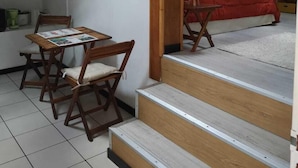 Une petite pièce, de dimensions réduites, avec un escalier en bois menant à une mezzanine. Une table à manger, entourée de chaises, est placée près de l’escalier.