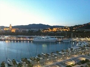 A marina with several boats docked, a large yacht, and buildings in the background.