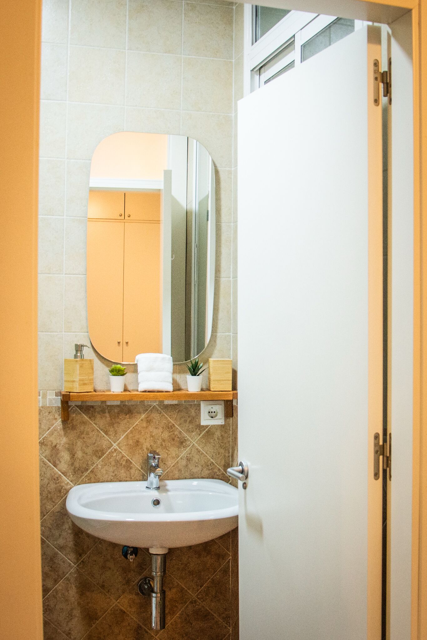 Un baño con lavamanos blanco, espejo y repisa de madera con artículos de aseo.