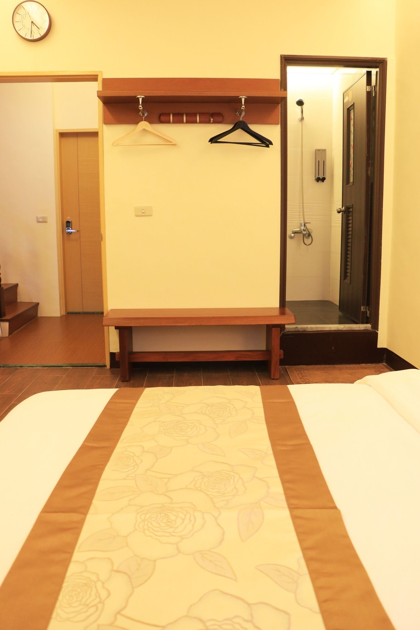 Habitación de hotel con cama, un banco de madera, perchero y baño visible a través de una puerta abierta.