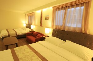 Habitación de hotel con dos camas, un sofá rojo, una mesita y una mesita de noche con una lámpara.