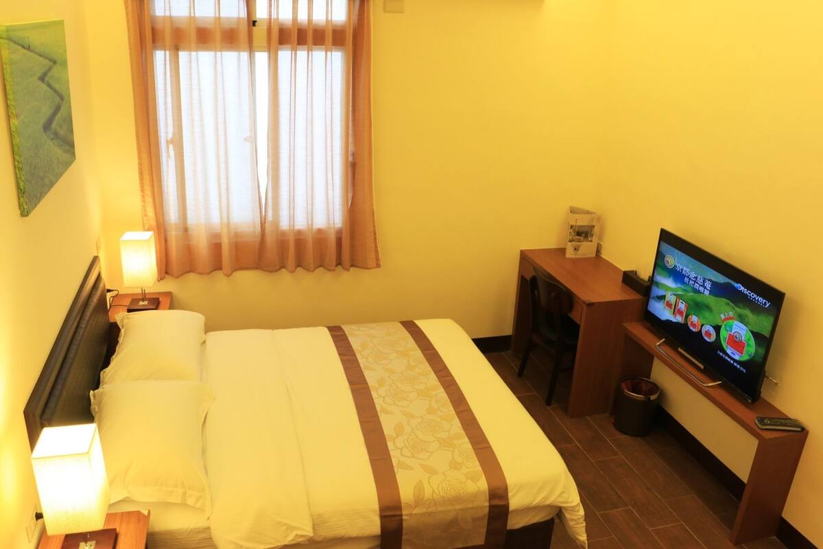 A hotel room with a bed, a desk, a television, and a window with curtains.