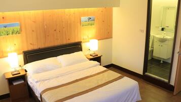 A neatly made bed with white linens and a brown stripe, flanked by two bedside tables with lamps, in a room with wooden paneling and a visible bathroom door.