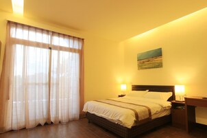 Habitación de hotel con una cama grande, dos lámparas de noche, una mesita de noche, un escritorio y un cuadro en la pared.