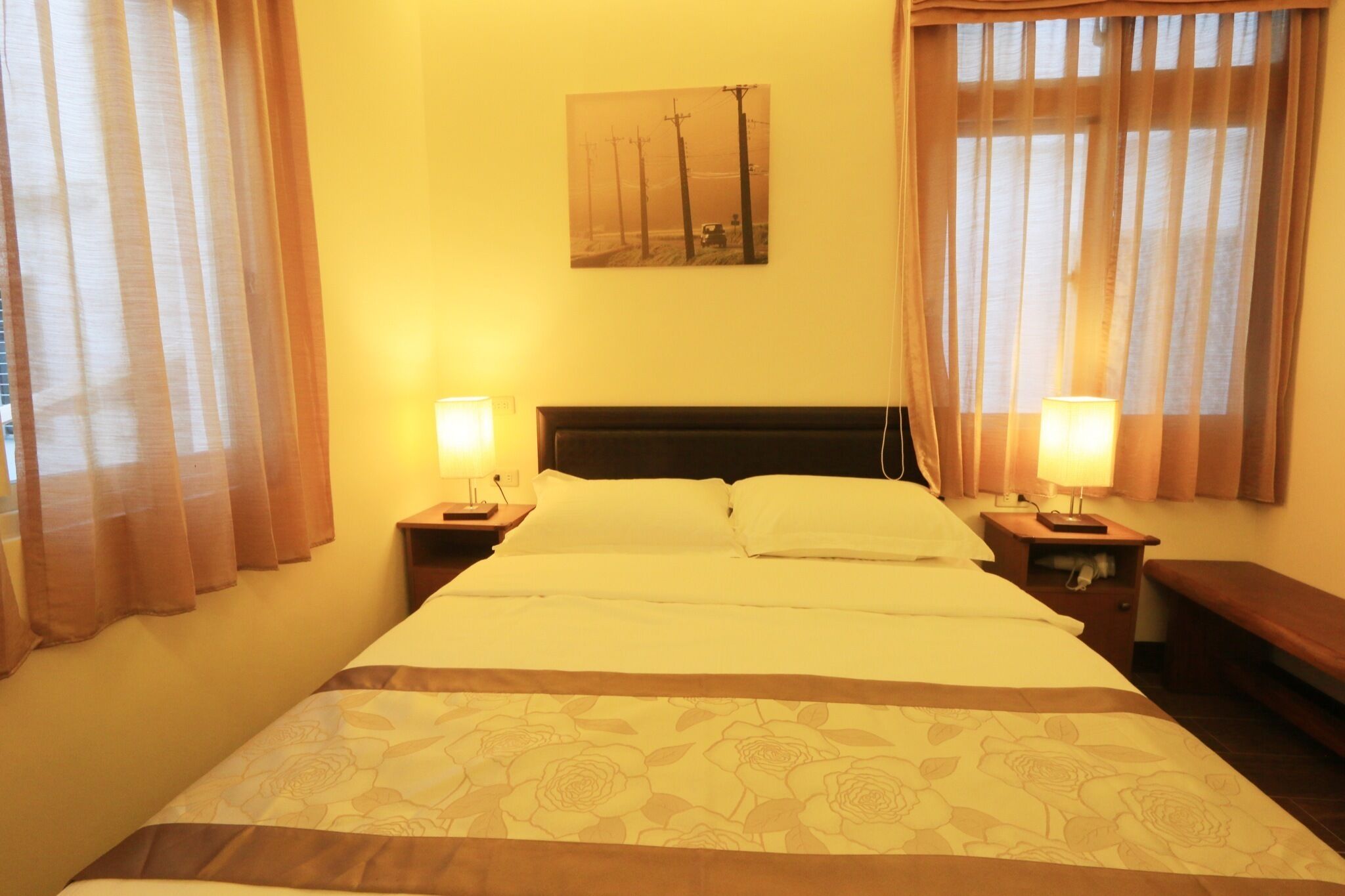 A hotel room with a large bed, two bedside tables with lamps, a headboard, and a painting on the wall.