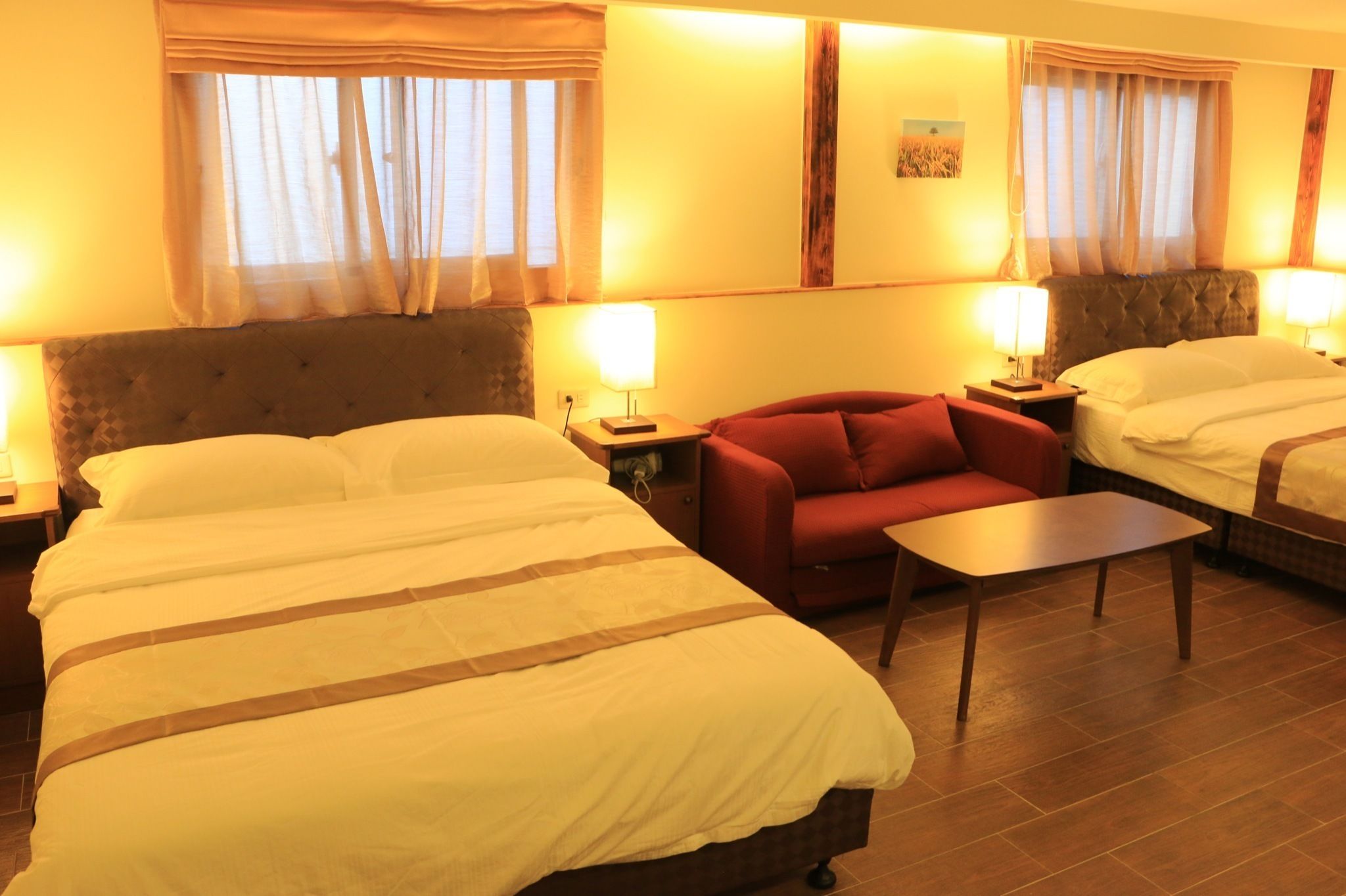 A hotel room with two beds, a sofa, a small table, and two bedside lamps.