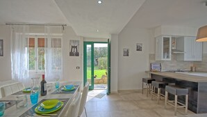 Una cocina moderna con comedor, que cuenta con un amplio ventanal, una puerta verde que da al exterior y una barra con taburetes.
