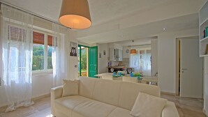 Una sala de estar con un sofá color beige, un comedor con una mesa dispuesta para dos personas y una cocina visible a través de una puerta abierta.