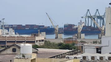 A port with large shipping containers and cranes, buildings with flat roofs, and a clear sky.