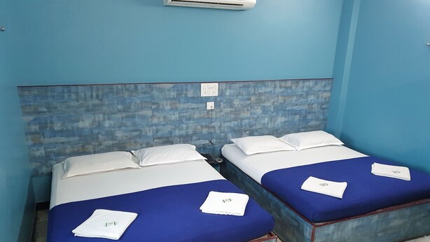 Una habitación con dos camas, cada una con un colchón azul y ropa de cama blanca. Hay un aire acondicionado instalado en la pared sobre las camas.