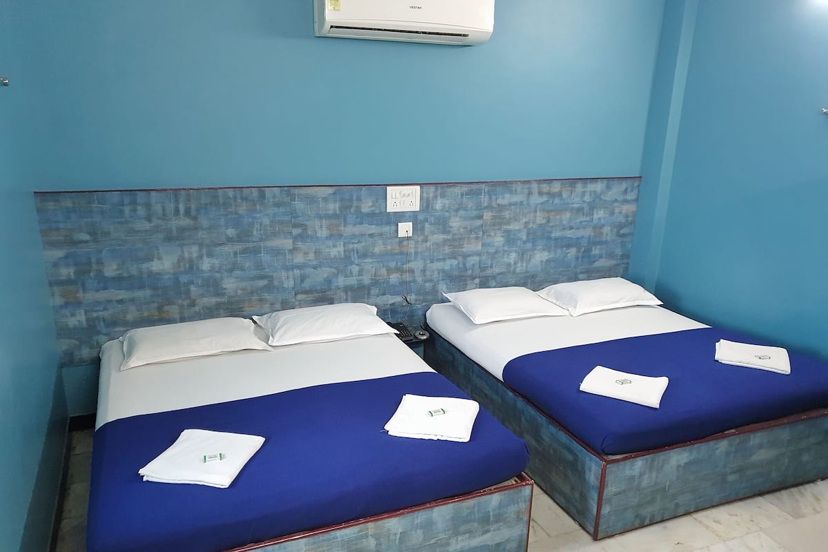 Una habitación con dos camas, cada una con un colchón azul y ropa de cama blanca. Hay un aire acondicionado instalado en la pared sobre las camas.