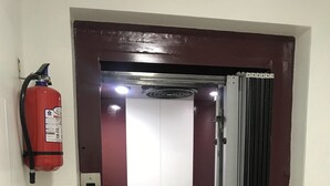 Un ascensor con una pared a rayas rojas y blancas, un extintor montado en la pared y un panel de control digital.