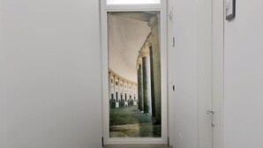 Un couloir étroit, doté d’un plancher sombre, de murs blancs et d’une porte sur le côté droit.