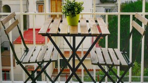 Un balcon avec une table en bois et deux chaises, un pot de fleurs et une vue sur un immeuble blanc doté de balcons.