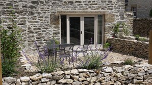 A stone building with a patio area featuring a table and chairs, surrounded by a stone wall and plants. - The Old Farmhouse - 2 Bedroom property, stunning character, views & location (Derbyshire)
