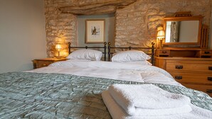 A bed with a stone wall behind it, a framed picture on the wall, and a wooden dresser with a mirror. - The Old Farmhouse - 2 Bedroom property, stunning character, views & location (Derbyshire)