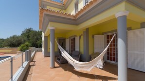 Ein überdachter Außenbereich mit einer Hängematte, einem Pool und einer Terrasse mit Möbeln.