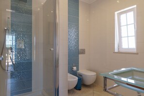 Un baño con cabina de ducha de vidrio, lavamanos de vidrio y un inodoro.