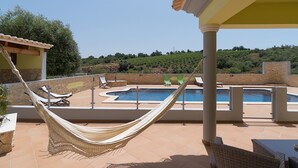 Ein Poolbereich mit einer Hängematte, Liegestühlen und Blick auf eine hügelige Landschaft.