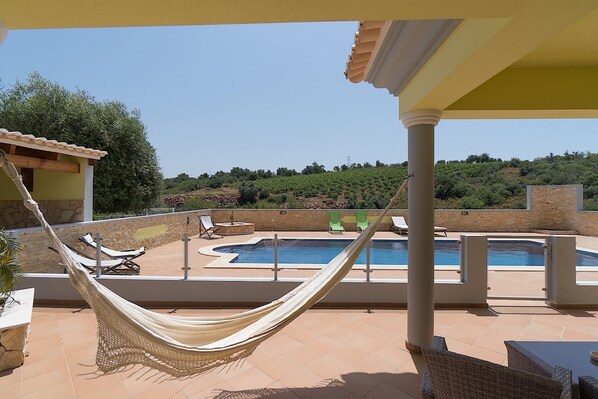 A pool area with a hammock, lounge chairs, and a view of a hilly landscape.