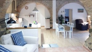 Una sala de estar acogedora con un sofá blanco, un comedor con mesa y sillas, y una cocina al fondo.