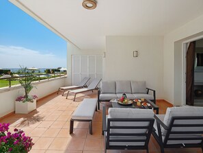 A balcony with a sofa, chairs, a table with food, and a view of the sea.