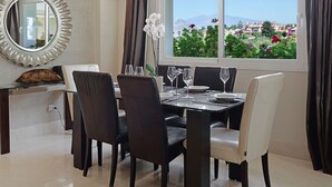 A dining area with a table set for four, a chandelier, a large mirror, and a window with a view of greenery and buildings. - 322 Luxury Apartments-Estepona, 2 b'room Apt, 28c All Year 20m Heated Pool (Estepona)