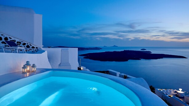 A pool with a view of the sea and islands, a white building with a balcony, and a sunset sky. - Nautilus,3 bedroom character villa with outdoors jacuzzi and fantastic sea views (Firostefani)