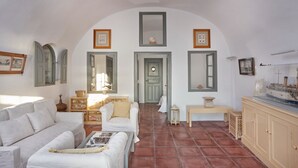A living room with a white sofa, a coffee table, and a cabinet. There is a door with a mirror above it, and a ship model on the right side. - Nautilus,3 bedroom character villa with outdoors jacuzzi and fantastic sea views (Firostefani)